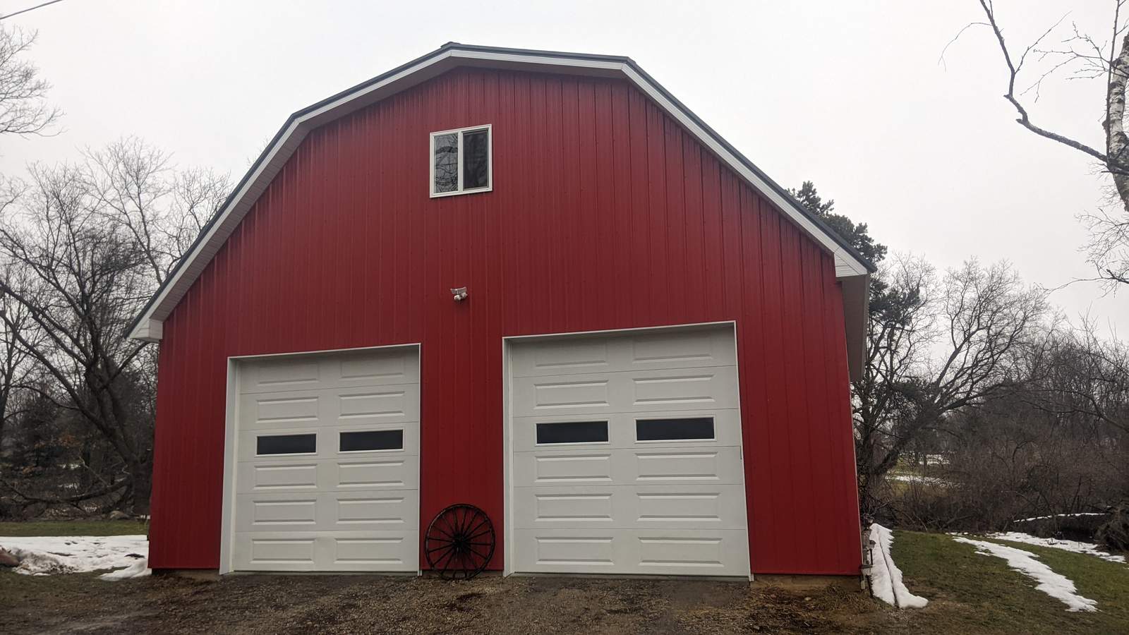 Red gambrel-roof pole barn with two white overhead doors